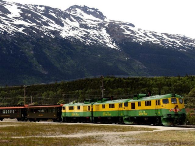 The White Pass & Yukon Route Railroad departs from Skagway, Alaska, toward White Pass summit, as passengers view cascading waterfalls, rugged mountain peaks, and wildlife from their open-air windows.